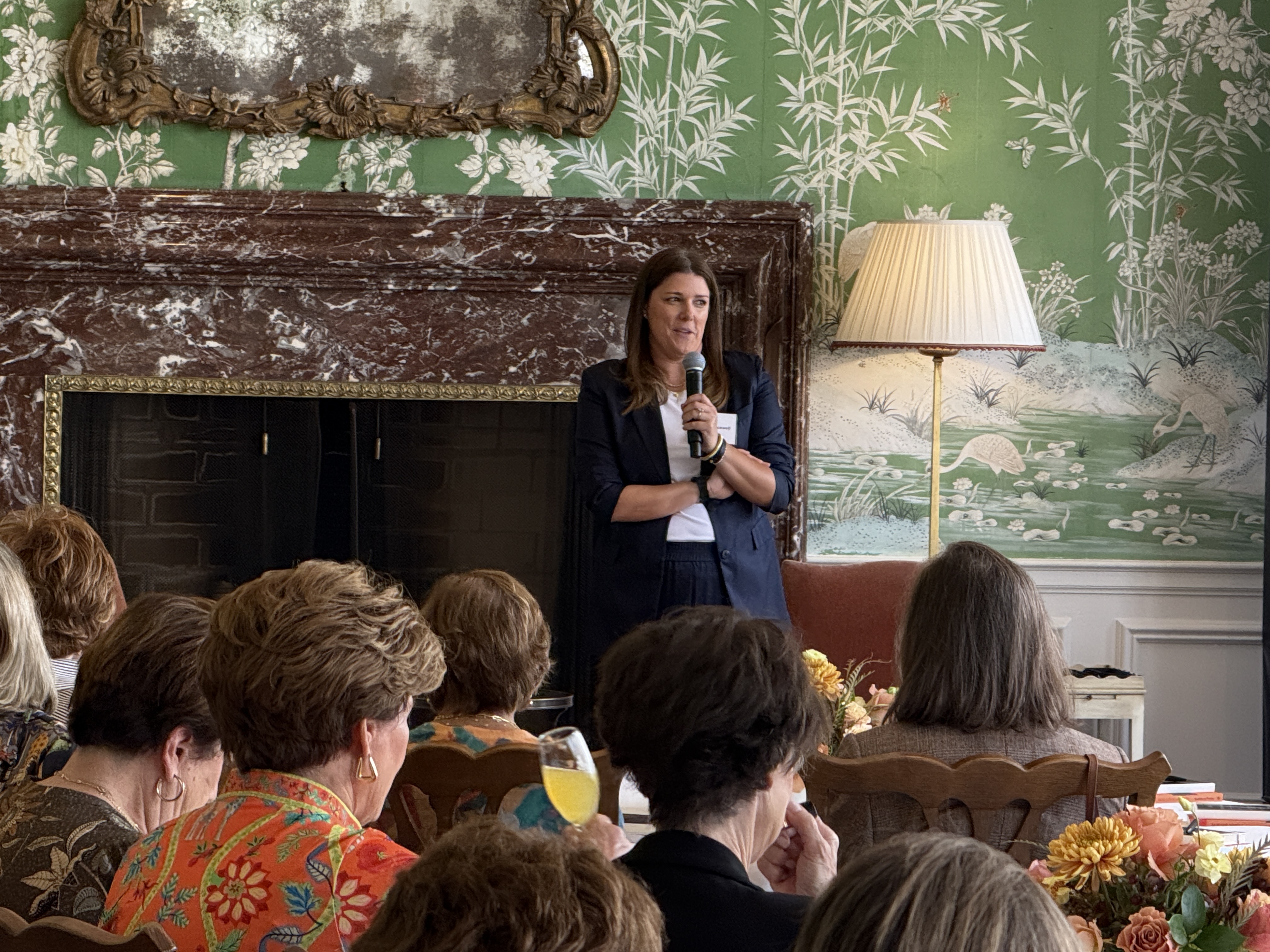 Speaker presenting in front of a dark marble fireplace, spectators seated